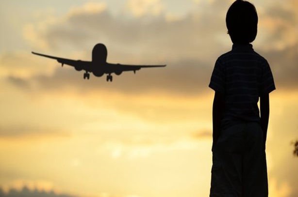 Silhueta de criança observando avião decolar ao pôr do sol, símbolo da adoção internacional e da mudança de país