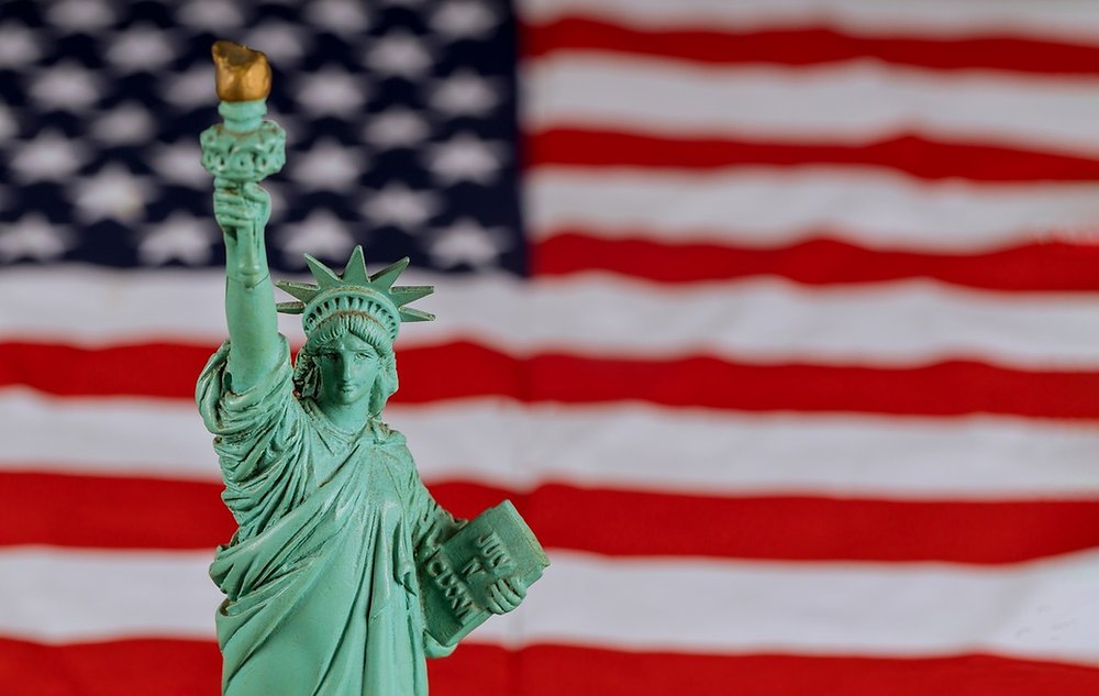Miniatura da Estátua da Liberdade diante da bandeira dos Estados Unidos, rotina de morar no país